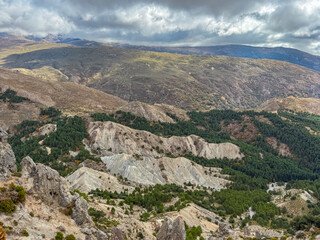 Obraz premium Scenic landscape featuring eroded white hills and pine forests stretching across the valley below Cerro del Trevenque in Sierra Nevada, Granada, Spain under a dramatic and moody cloudy sky.
