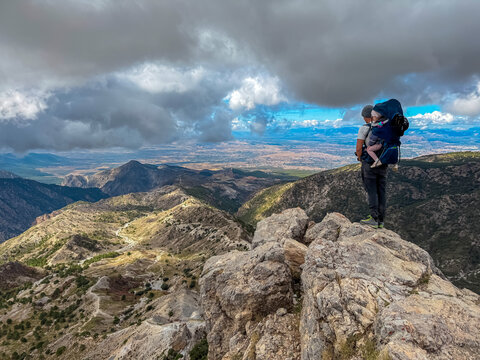 Hiker with a child carrier pauses on a rocky peak to overlook the sweeping valleys of Cerro Del Trevenque in Sierra Nevada, Spain, enjoying the freedom and nature of the mountainous Granada landscape