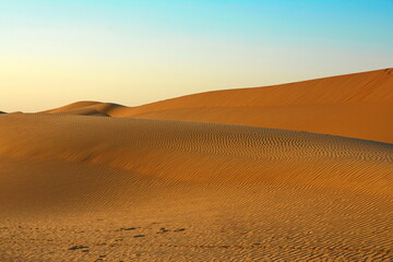 Sunset over the desert of Al Khatim in Abu Dhabi, Emirates. Golden Sand Dune desert landscape dunes with blue sky. Sand mounds formed in circular shape, beauty of natural changes over great stretches