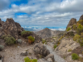 Scenic view of the rugged Cerro del Trevenque peak rising above arid slopes and green shrubs under a cloudy sky in Sierra Nevada, capturing the wild beauty of the Andalusian mountain landscape.