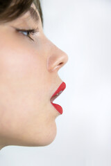 Side profile close up of woman face with red lipstick open mouth clean skin and sharp nose line creating minimalist beauty makeup concept