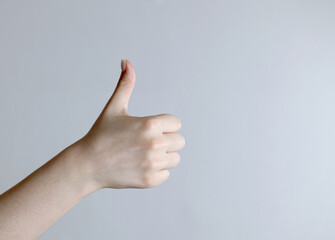 Hand giving thumbs up gesture on on grey background