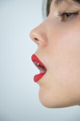 Side profile close up of woman face with red lipstick open mouth clean skin and sharp nose line creating minimalist beauty makeup concept
