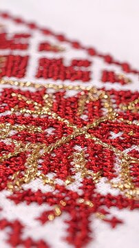 Macro view of an intricate red and gold thread embroidery on white fabric. The traditional, festive pattern resembles a snowflake