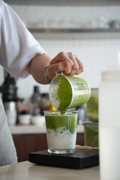 barista pouring matcha over milk, making iced matcha latte in a cafe