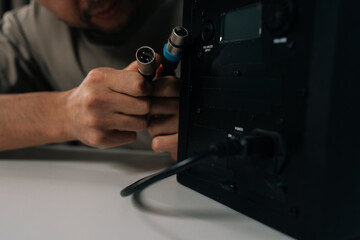 Hand of sound engineer male connecting professional xlr audio cable into balanced input of black studio monitor speaker, setting up equipment for music recording and sound engineering.