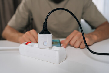 Cropped shot of person wirelessly setting up smart socket device plugged into power strip, interacting with smartphone display for home automation and remote control of appliances.