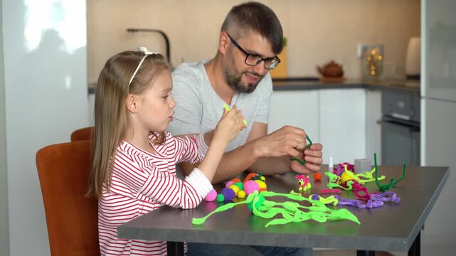 Happy family father and little girl create handmade craft from colored chenille wire toys. Diy. Leisure with children. Education