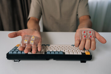 Man holding mechanical keyboard switches, choosing between different types for custom keyboard building and maintenance, repairing personal computer hardware, cropped shot portrait.