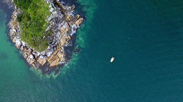 high-altitude drone shot of a lush green islet surrounded by clear tropical water and a small vessel