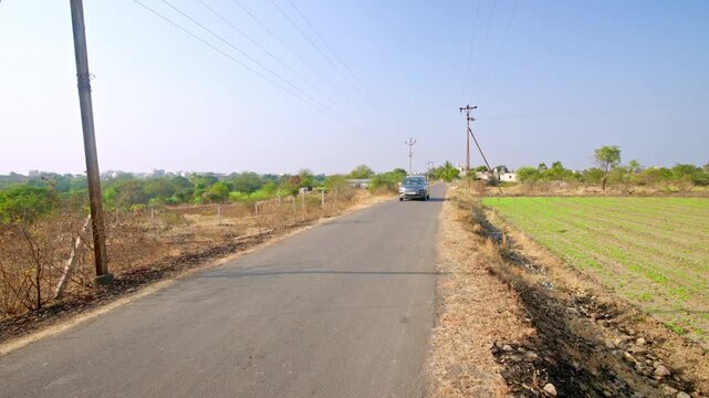 Car passing on rural tar road through agricultural fields, India countryside