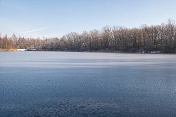 Icebound lake with trees around during freezing winter day