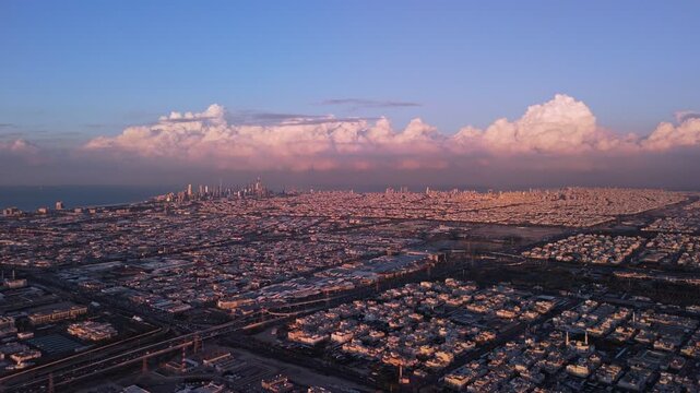 Wide drone view of Kuwait City at golden hour,distant downtown on the Gulf coast, vast residential sprawl, and a towering cumulonimbus line warm sunset light, clear visibility, clean establishing shot