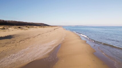 Aerial view of empty sandy beach and calm sea under clear blue sky. Peaceful coastline with gentle waves, dunes and distant horizon, ideal for travel, nature and relaxation themes