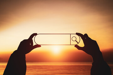 Silhouette of hand holding a search bar against sunset background. Concept of SEO and data discovery.