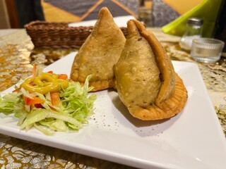 Traditional samosas with flaky crust and aromatic filling, served with dipping sauces on a rectangular plate, perfect for lunch or snack concept.
