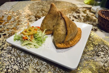 Golden fried samosas with crunchy pastry, filled with spiced vegetables, accompanied by green chutney and sweet sauce on a wooden table.