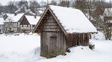 Wooden shed covered in snow, surrounded by a winter landscape and traditional buildings. Ideal for seasonal themes, winter sports, or rural photography.