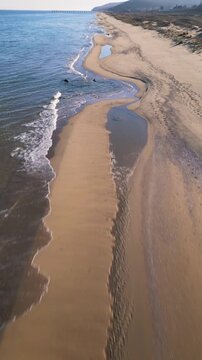 Aerial view of empty sandy beach and calm sea under clear blue sky. Peaceful coastline with gentle waves, dunes and distant horizon, ideal for travel, nature and relaxation themes