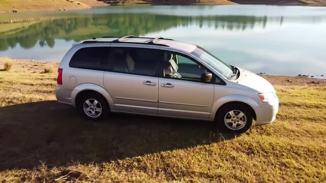 Silver minivan parked by the lake, showcasing travel, transport and outdoor lifestyle in a nature landscape setting.