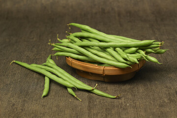 Fototapeta premium Fresh green beans in a wicker container with a wooden textured background.