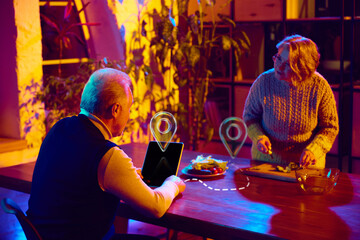 Senior couple cooking at home while planning trips with digital assistant. Concept of smart home control, AI communication, travel planning, modern retirement lifestyle, and assistive technology use.