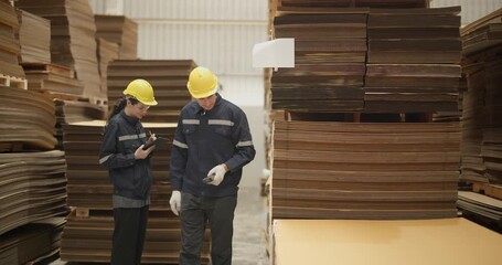 Workers in a cardboard warehouse conducting an inventory check, wearing safety gear amidst organized stacks of cardboard boxes.
 - Powered by Adobe
