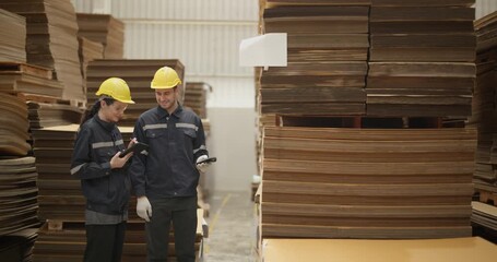 Workers in a cardboard warehouse conducting an inventory check, wearing safety gear amidst organized stacks of cardboard boxes.
 - Powered by Adobe