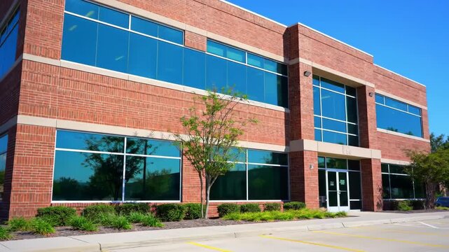 A modern brick office building with reflective blue windows on a sunny day in a business park featuring clear blue sky and lush green landscape.