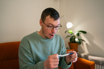 Man holding a pregnancy test, expressing surprise and shock, reacting to unexpected news about an unplanned pregnancy and contemplating the emotional implications of becoming a father