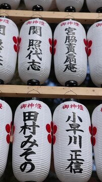 Rows of traditional white Japanese paper lanterns with black calligraphy hanging at a shrine during a festival in Japan