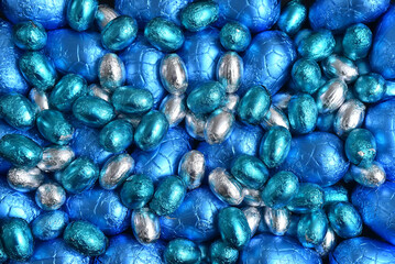 Blue,  silver and turquoise foil wrapped chocolate easter eggs, against a black background.
