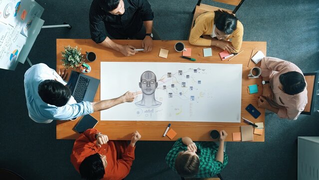 A diverse group collaborates in a creative meeting setting, utilizing charts and notes on a large wooden table, fostering innovation and strategic discussions. Raster - Powered by Adobe