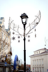 street lamp adorned with decorative star-shaped ornaments and wing-like structures set against an urban backdrop of elegant architecture under a bright, clear sky, simplicity, atmosphere