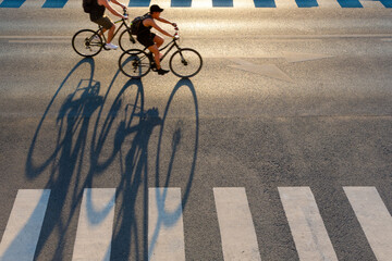 Two bicyclists in motion with long shadow on the road