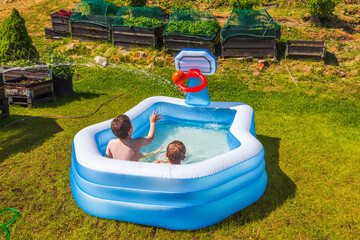 Beautiful summer backyard view with children playing in inflatable pool during outdoor water fun. Sweden.