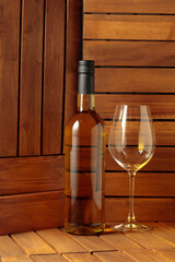 Bottle and glass of white wine on a wooden background.