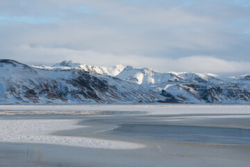 Amazing winter landscape near Reynisfjara beach. Water surrounded with ice, partial frozen sea, snowy mountains in the background. Cold frozen winter landscape in Iceland, Europe. Pristine landscape.