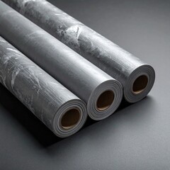Fototapeta premium Three rolls of gray, marble-patterned material, likely vinyl or wallpaper, rest on a gray surface