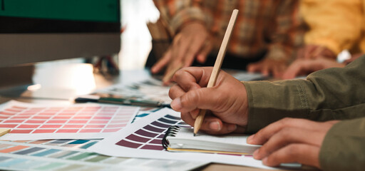 A group of diverse designers collaborates in a bright workspace, using color samples and sketching tools to brainstorm creative ideas and innovative projects. SACTR