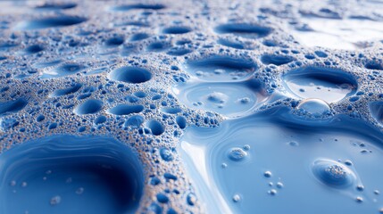 Glossy blue liquid droplets and puddles on rough gray textured surface, shimmering with metallic reflections and viscosity, creating a striking contrast between smooth fluid and gritty background