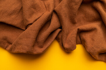 Close-up of wrinkled brown cotton fabric on yellow backgroud top view. Waves of natural, eco-friendly fabric, abstract background of clothing material. Cotton fabric texture, textile industry, fashion