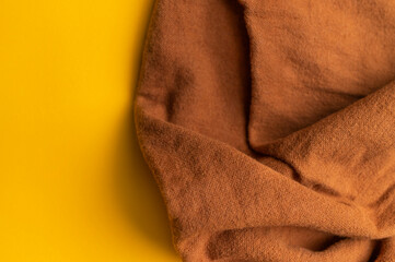 Close-up of wrinkled brown cotton fabric on yellow backgroud top view. Waves of natural, eco-friendly fabric, abstract background of clothing material. Cotton fabric texture, textile industry, fashion