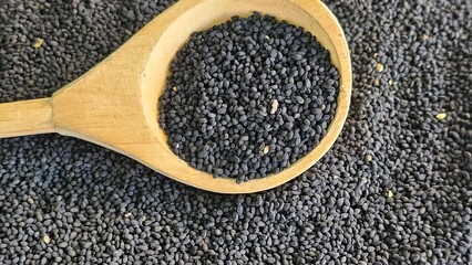 Black cumin seeds in a wooden spoon with other black seeds in a market background concept