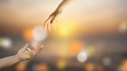 Two hands are reaching out to each other against a blurred golden sunset backdrop. Symbolizing connection, love, support, and the desire to help. Sense of hope, faith, and reaching for a better future