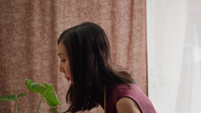 Young Asian dark-haired woman in dress offering prayers by home altar with Buddha figurine, fruits, and flowers during Tet celebration