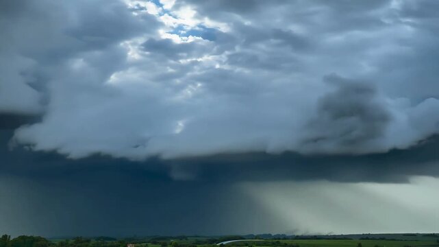 Powerful dark storm clouds moving over a green landscape with visible rain curtains falling from the sky in a dramatic weather event.