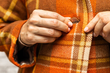  A woman buttoning her coat, close-up. A woman unbuttons her coat. women's fingers fastening a button. woman putting on coat. fingers fasten a button. woman trying on coat. 