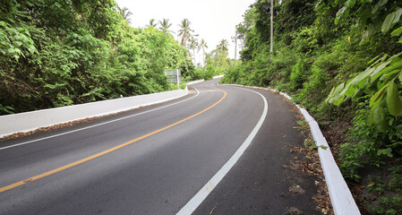 Road with a white line down the middle and a green hillside in the background