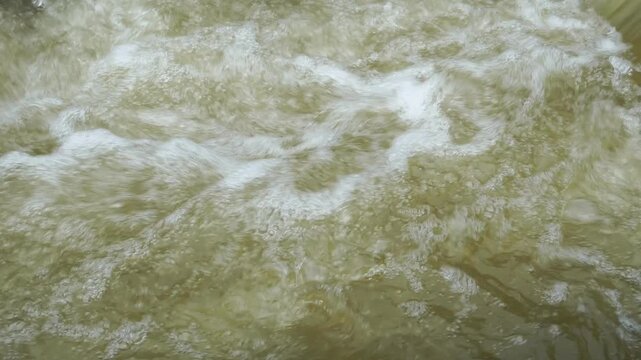 Close up abstract texture of murky brown river water flowing rapidly. Turbulent muddy stream surface with churning foam and ripples. Environmental pollution, flood water, or high sediment concept.